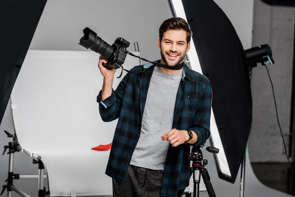 jovem fotógrafo bonito feliz segurando câmera de foto profissional em estúdio
 - Foto, Imagem