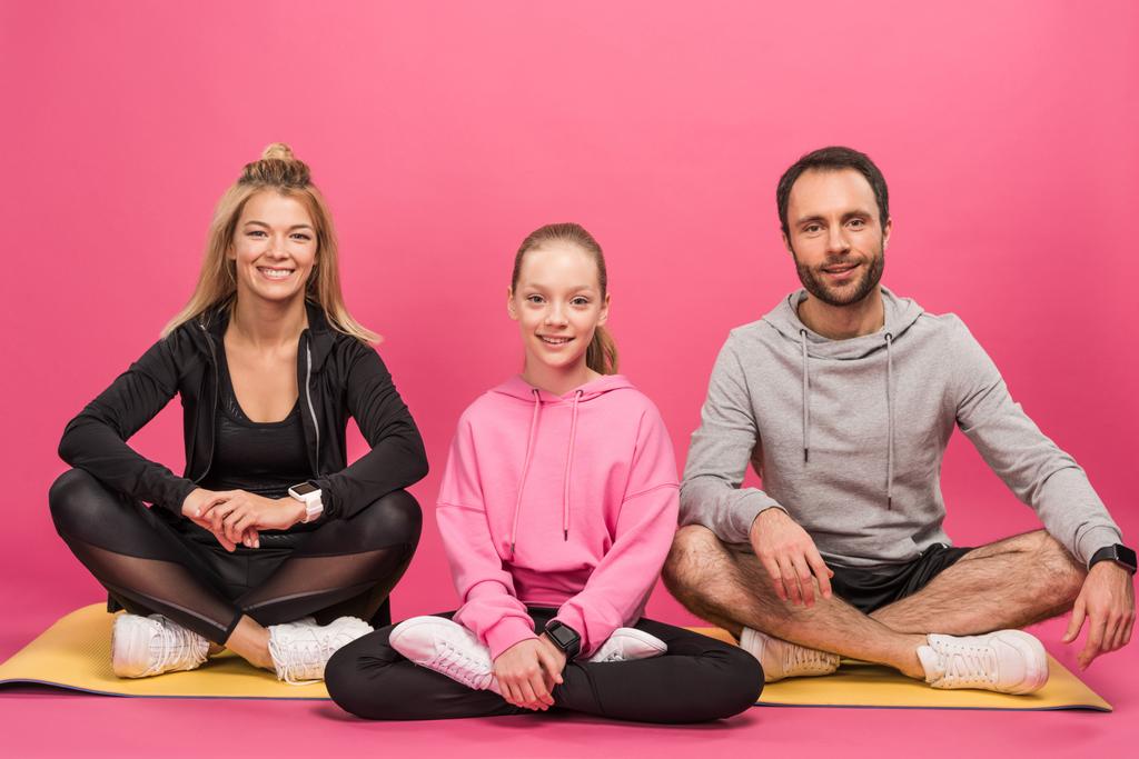 famiglia sportiva seduta sul tappeto fitness, isolata sul rosa
 - Foto, immagini