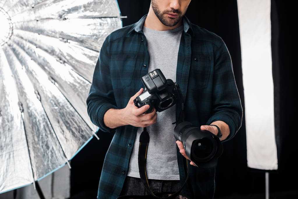 обрезанный снимок молодого фотографа с фотокамерой и объективом в студии
 - Фото, изображение