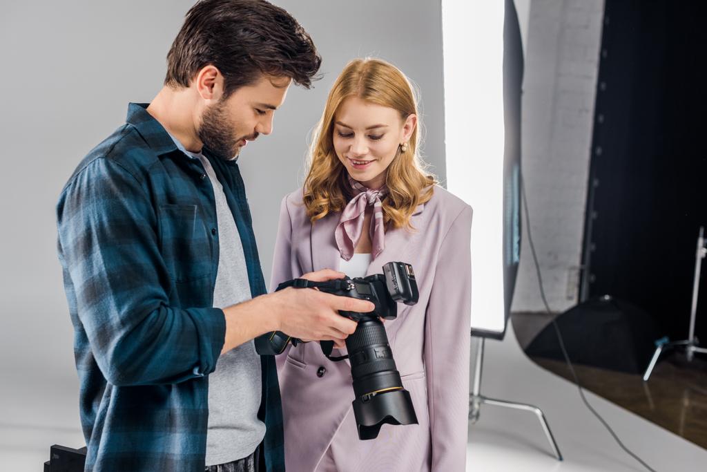 bonito jovem fotógrafo e sorridente fêmea modelo usando foto câmera juntos no estúdio
  - Foto, Imagem