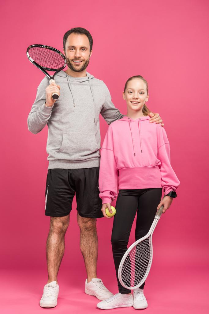 handsome father and daughter holding tennis rackets and ball, isolated on pink - Photo, Image