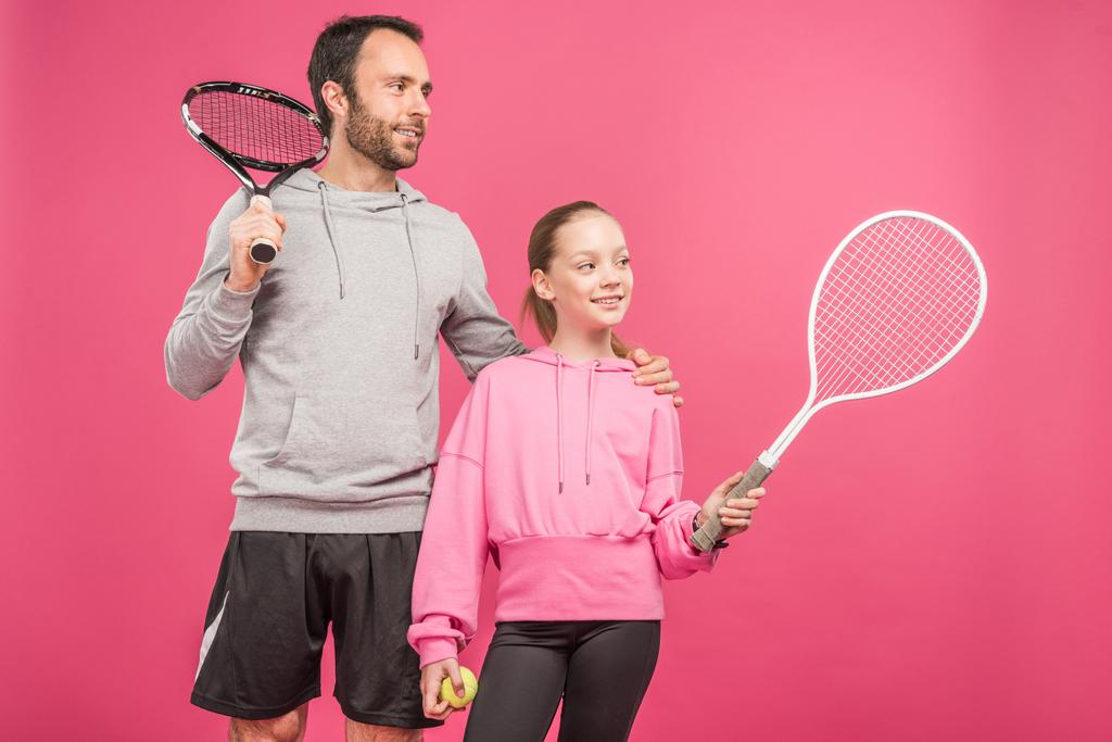 αθλητική πατέρας και preteen κόρη κρατώντας ρακέτες του τένις και μπάλα, απομονώνονται σε ροζ - Φωτογραφία, εικόνα