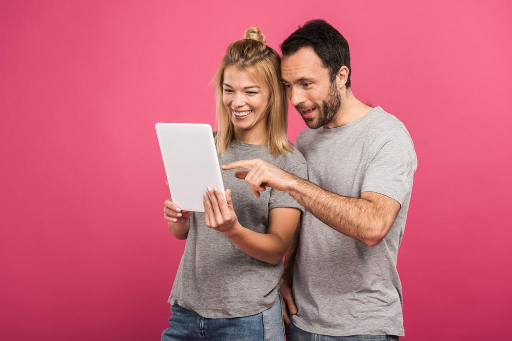 happy beautiful couple using digital tablet, isolated on pink - Photo, Image