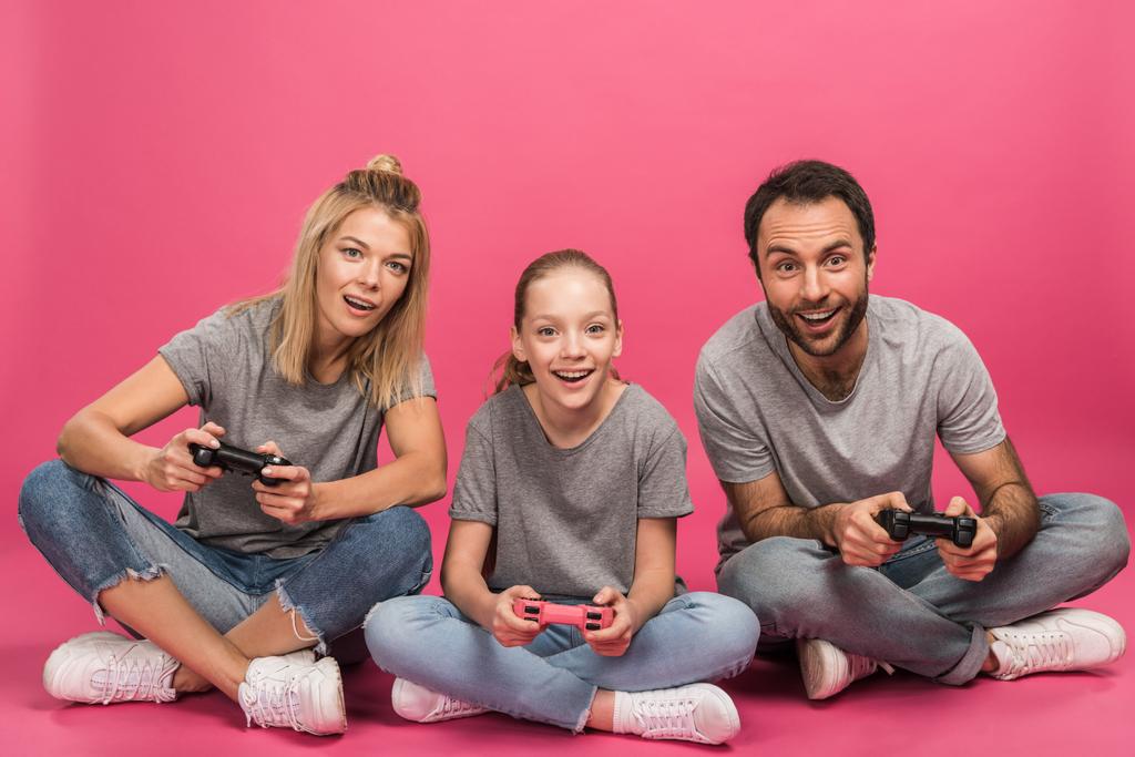 excited family playing video game with joysticks, isolated on pink - Photo, Image