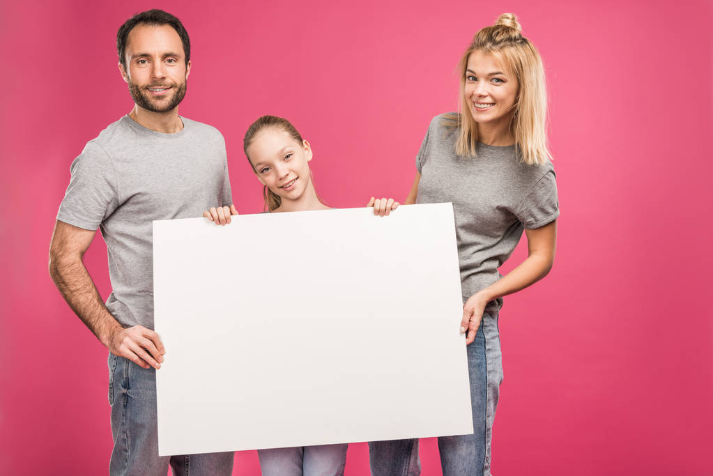 familia sonriente posando con tarjeta en blanco, aislado en rosa
 - Foto, imagen