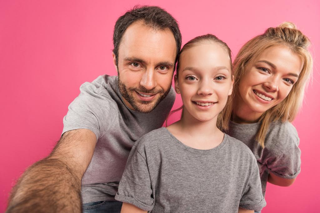 hymyilevä vanhemmat ja tytär ottaen selfie yhdessä, eristetty vaaleanpunainen
 - Valokuva, kuva
