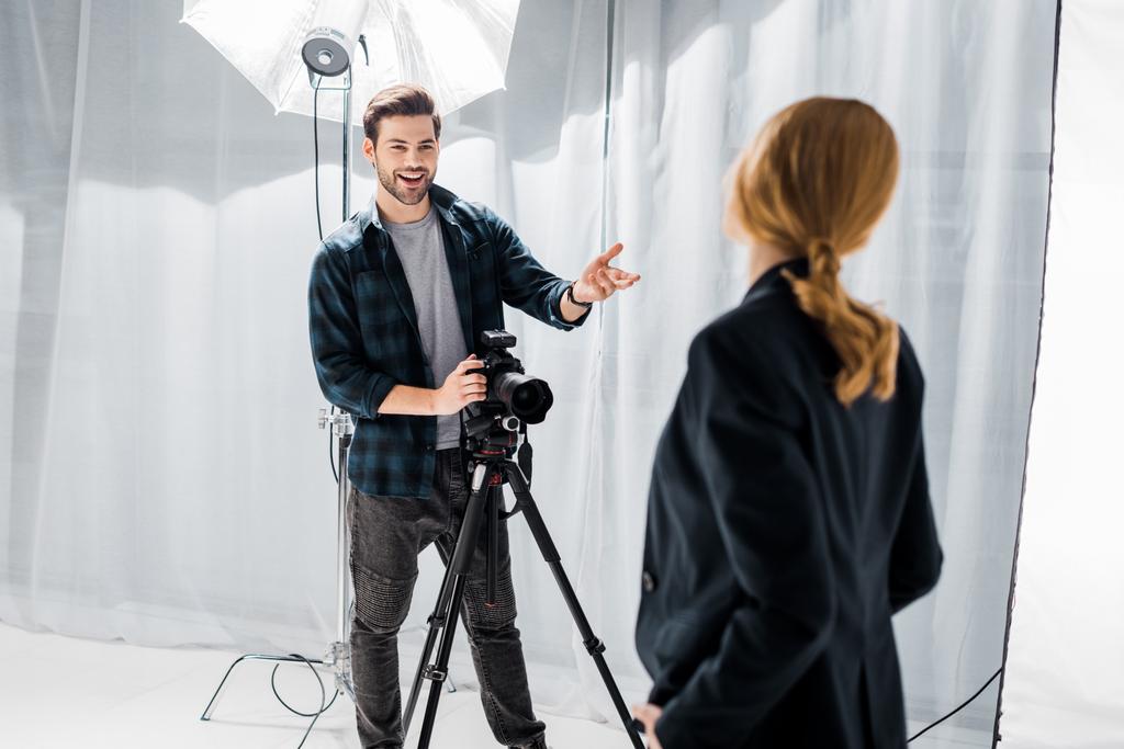 uśmiechnięty młody fotograf za pomocą aparatu i rozmowa z kobieta model w studio - Zdjęcie, obraz