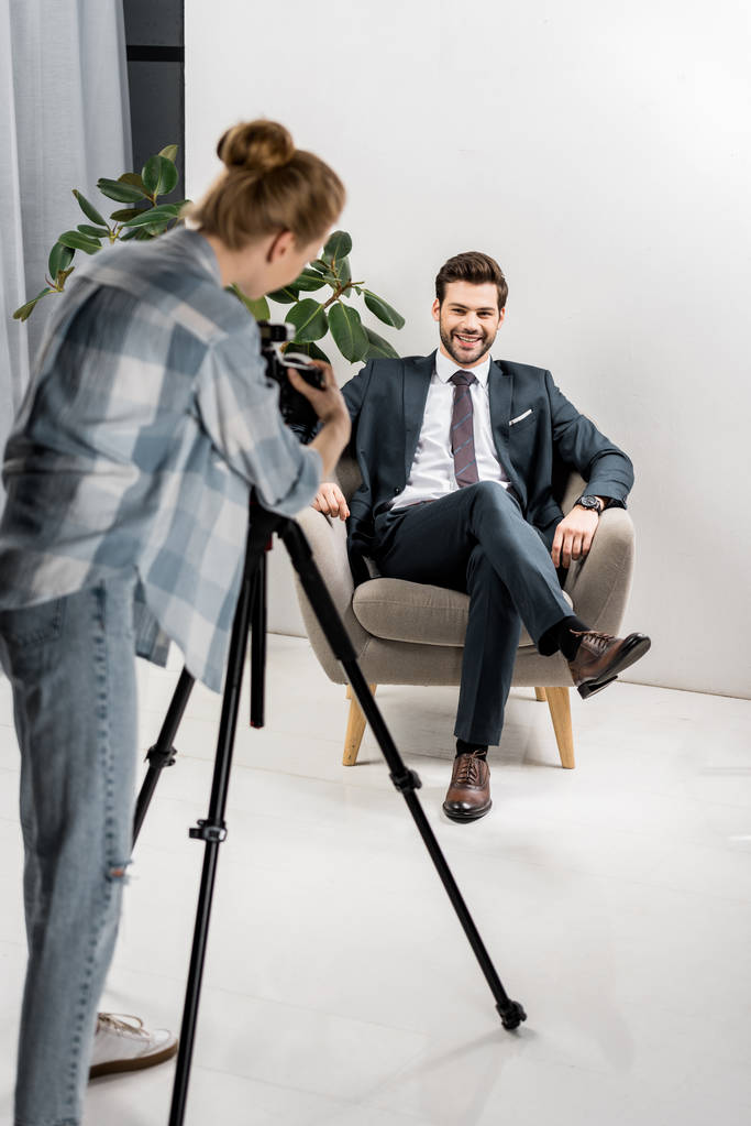 Rückansicht eines jungen Fotografen, der Fotos von gut aussehenden lächelnden Geschäftsmann im Büro macht - Foto, Bild