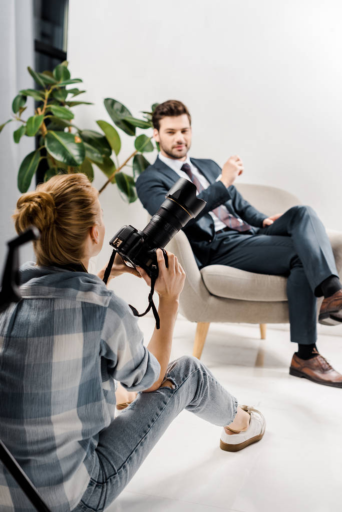 vista posterior de fotógrafa con cámara fotográfica fotografiando apuesto hombre de negocios en estudio
  - Foto, imagen