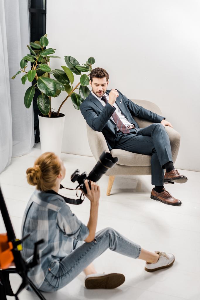 hoge hoekmening van jonge vrouwelijke fotograaf fotograferen knappe zakenman in studio - Foto, afbeelding