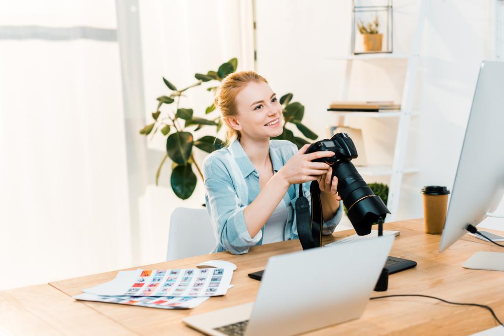beautiful smiling young female photographer holding camera while working in office  - Photo, Image