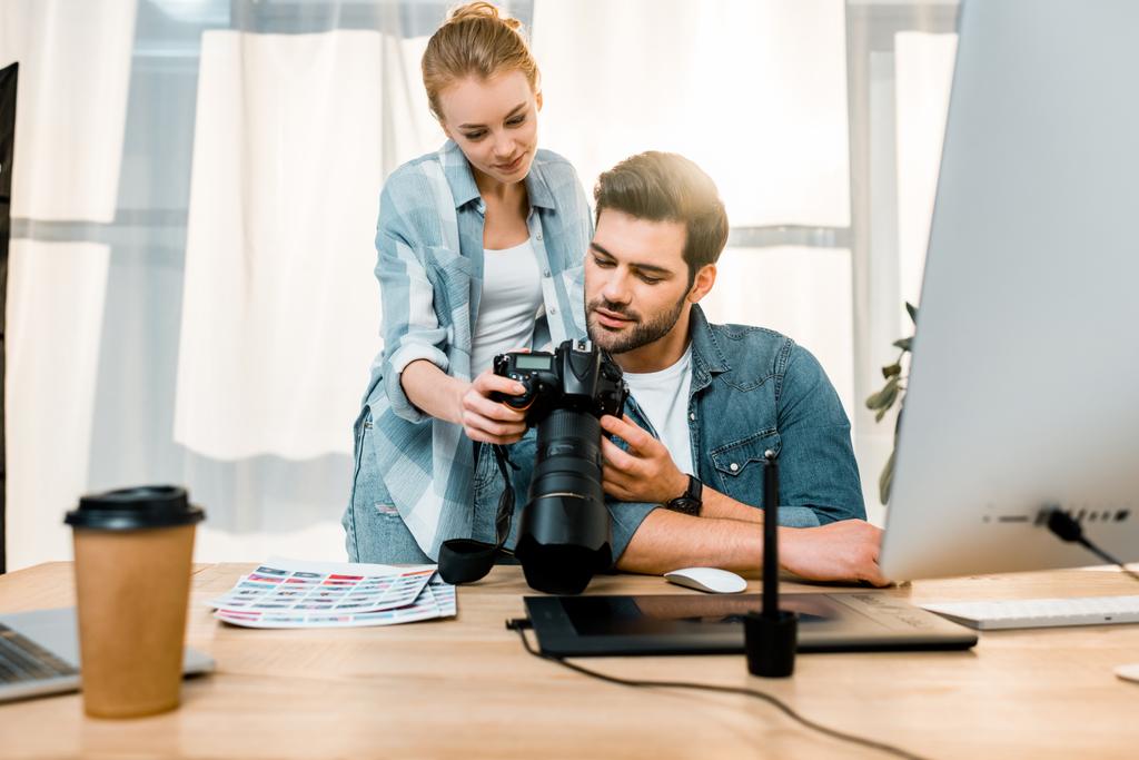 профессиональные улыбающиеся молодые фотографы, работающие с фотокамерой в офисе
 - Фото, изображение