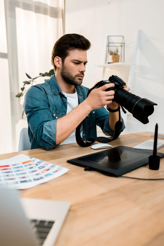 joven fotógrafo guapo usando cámara en el lugar de trabajo
   - Foto, Imagen