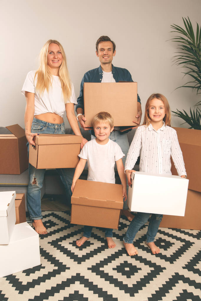 Full-length image of young married couple with children with cardboard boxes in their hands standing - Photo, Image