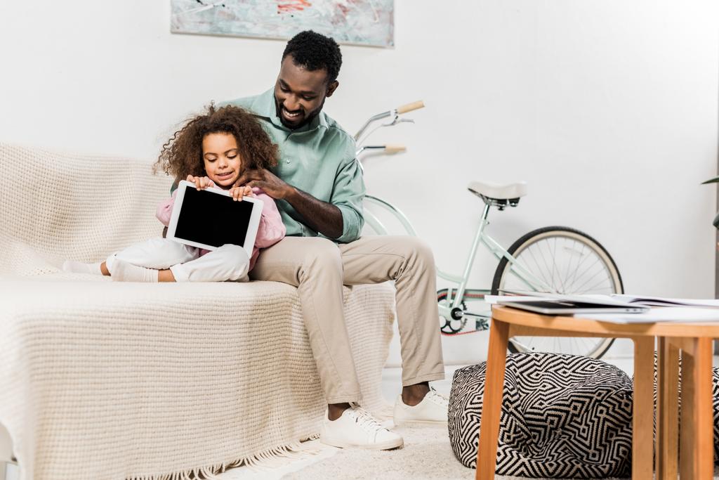 african american father and daughter sitting on couch in living room with digital tablet - Photo, Image