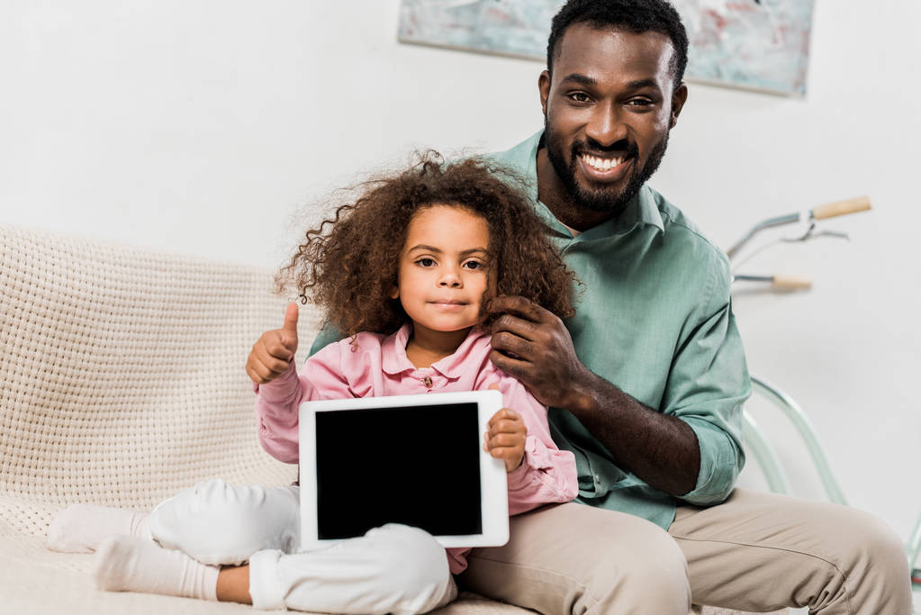 Αφρικανική αμερικανική πατέρας και κόρη κάθεται στον καναπέ με ψηφιακό tablet και βλέπουν τα φωτογραφικών μηχανών - Φωτογραφία, εικόνα