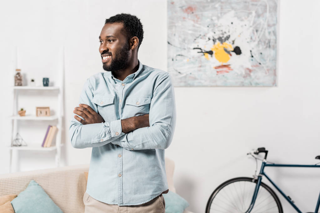 hombre afroamericano de pie con los brazos cruzados en sala de estar
  - Foto, Imagen