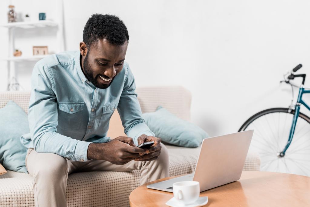 african american freelancer sitting on couch and typing on smartphone - Photo, Image