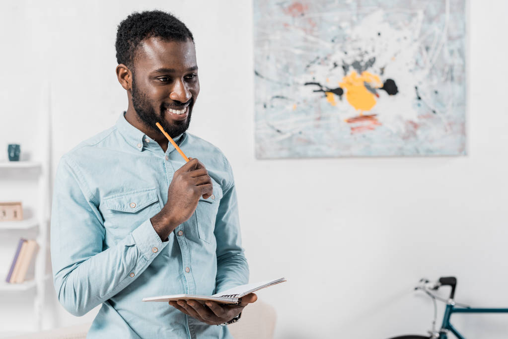 усміхнений афроамериканський чоловік тримає олівець і блокнот
 - Фото, зображення