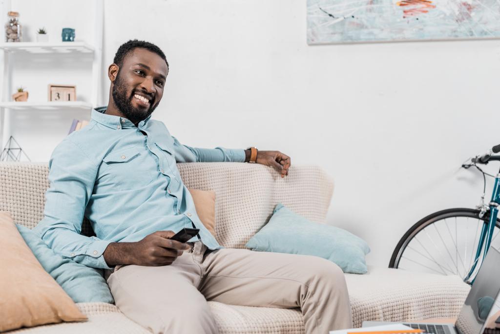 リモート コント ローラーとソファに座って満足しているアフリカ系アメリカ人 - 写真・画像