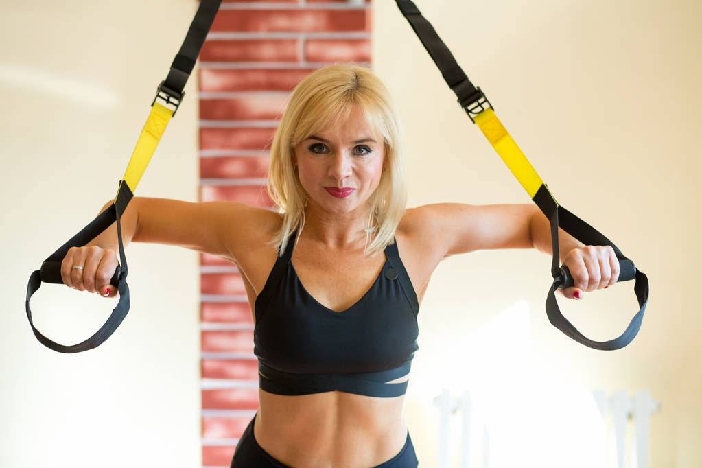 Portrét ženy středního věku dělá cvičení s kroužky ve fitness centru. - Fotografie, Obrázek