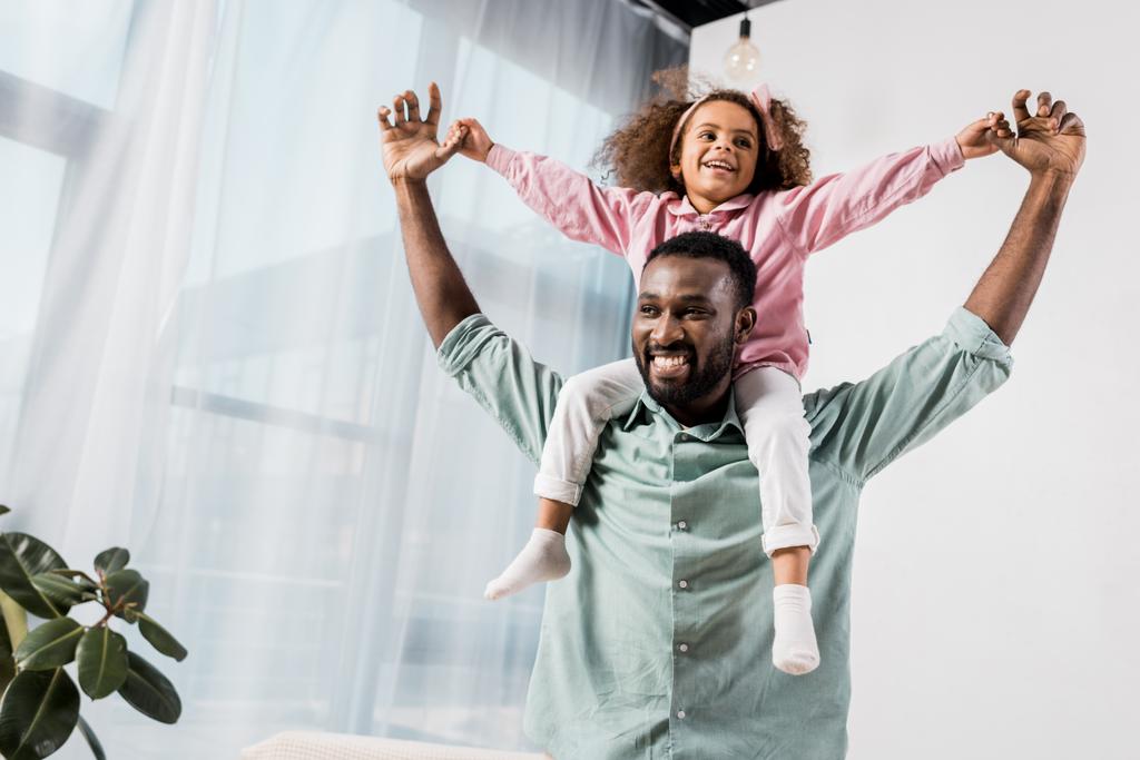 Afrikaanse Amerikaanse vader dochter uitvoering op hals en spelen in de woonkamer - Foto, afbeelding