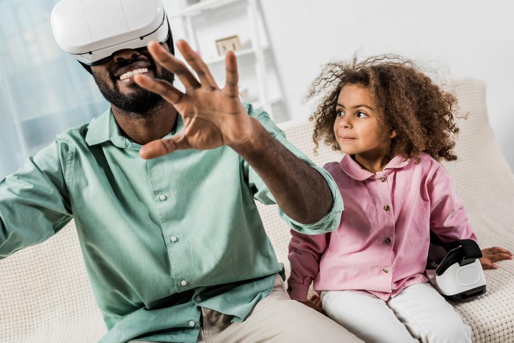 homme afro-américain avec des lunettes de réalité virtuelle et fille assise sur le canapé
 - Photo, image