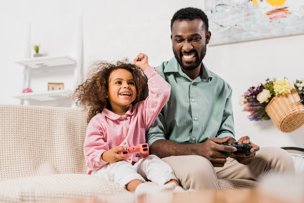 アフリカ系アメリカ人の父と娘のリビング ルームでジョイスティックとビデオ ゲームをプレイ - 写真・画像