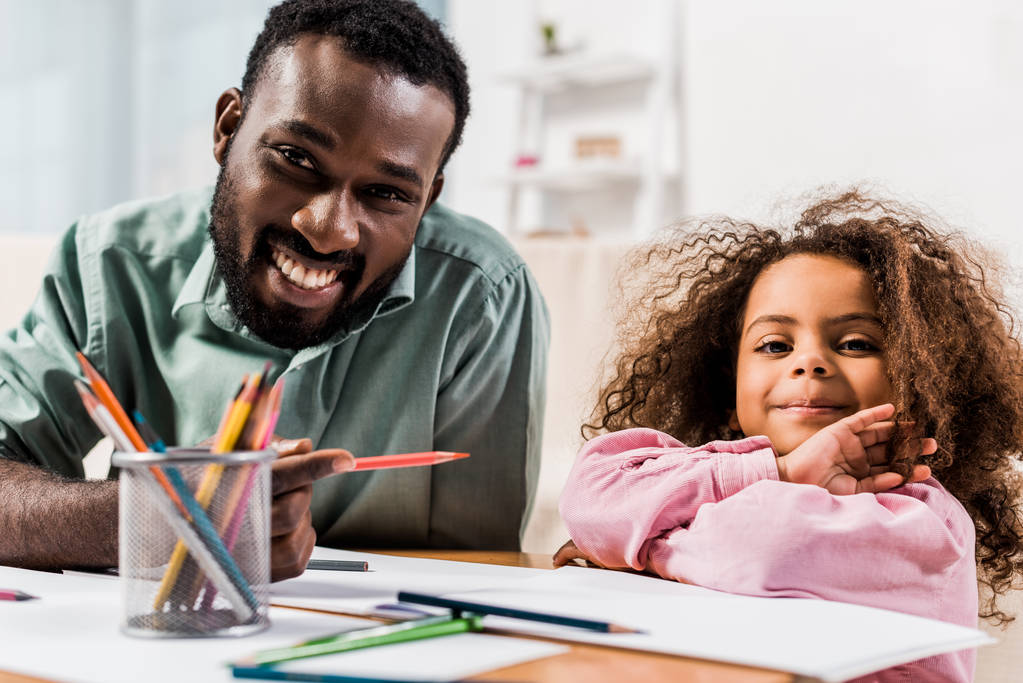 vista de cerca de papá afroamericano sosteniendo lápiz y ayudando a su hija con el dibujo en la sala de estar
 - Foto, imagen