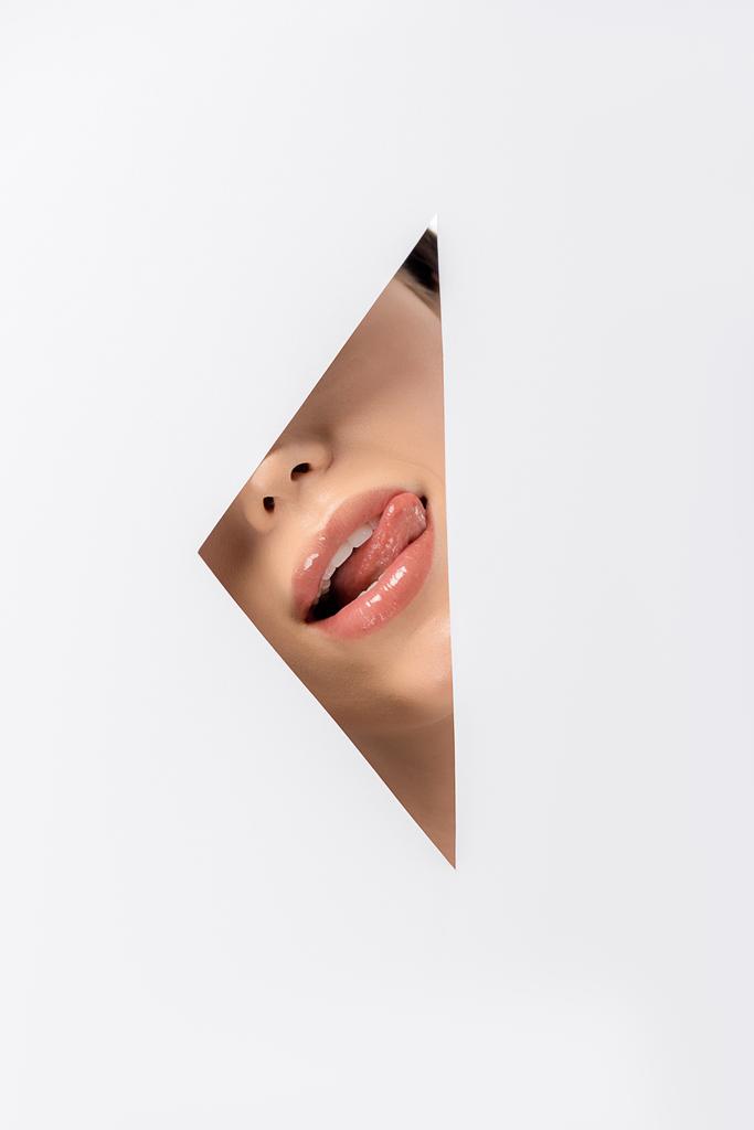 обрізаний знімок дівчини лиже губи через отвір на білому
 - Фото, зображення