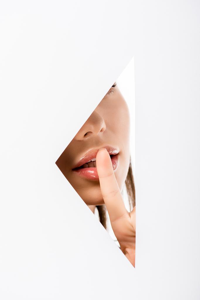 abgeschnittene Aufnahme einer jungen Frau, die durch ein Loch auf Weiß zum Schweigen gestikuliert - Foto, Bild