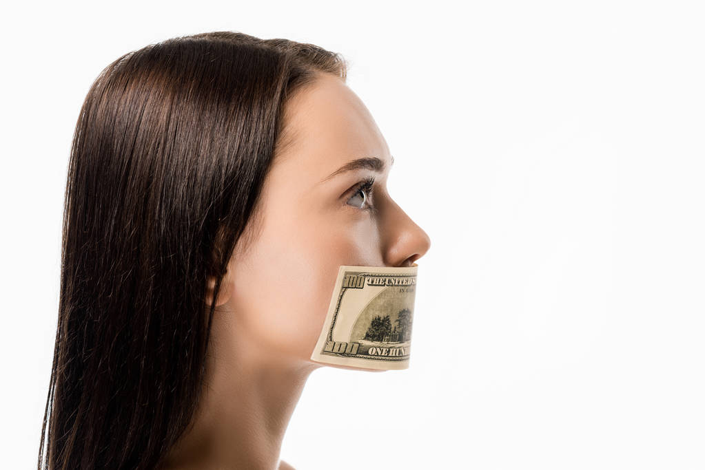 Seitenansicht einer Frau mit Dollarschein auf dem Mund, die isoliert auf weißem Grund wegschaut  - Foto, Bild
