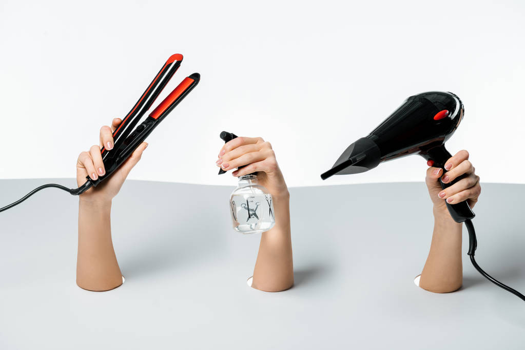 visão parcial de mulheres segurando ferramentas de penteado através de furos no branco
 - Foto, Imagem