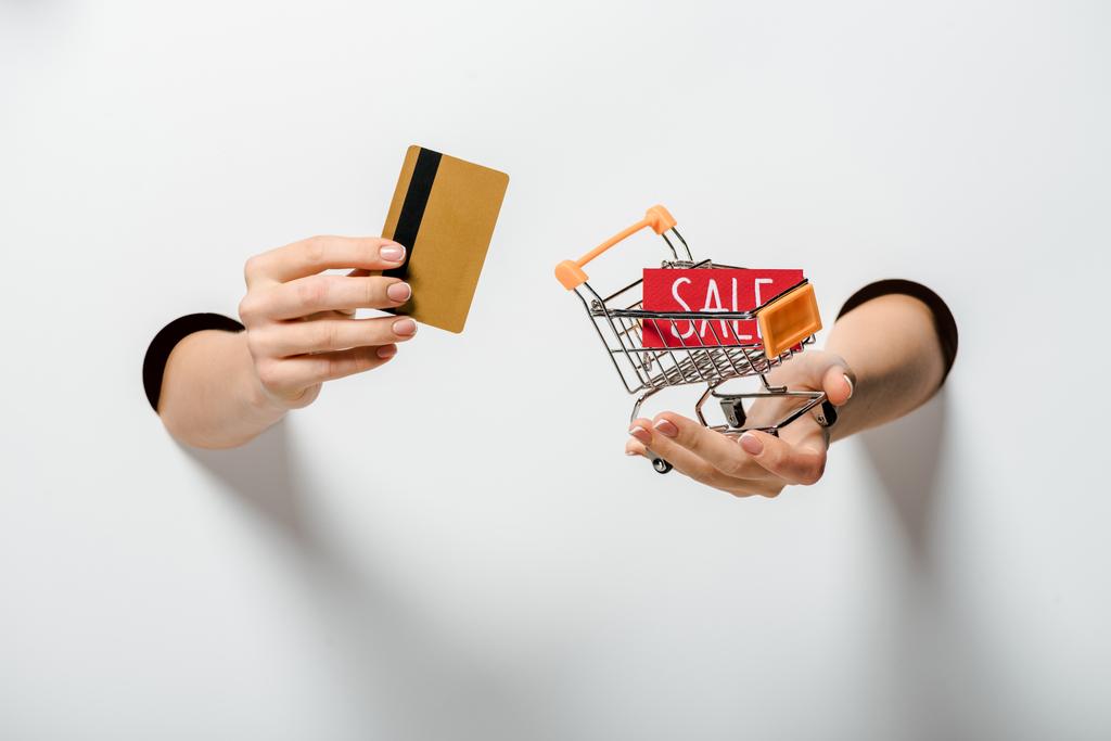 abgeschnittenes Bild einer Frau mit kleinem Einkaufswagen und Kreditkarte auf weißem Hintergrund - Foto, Bild