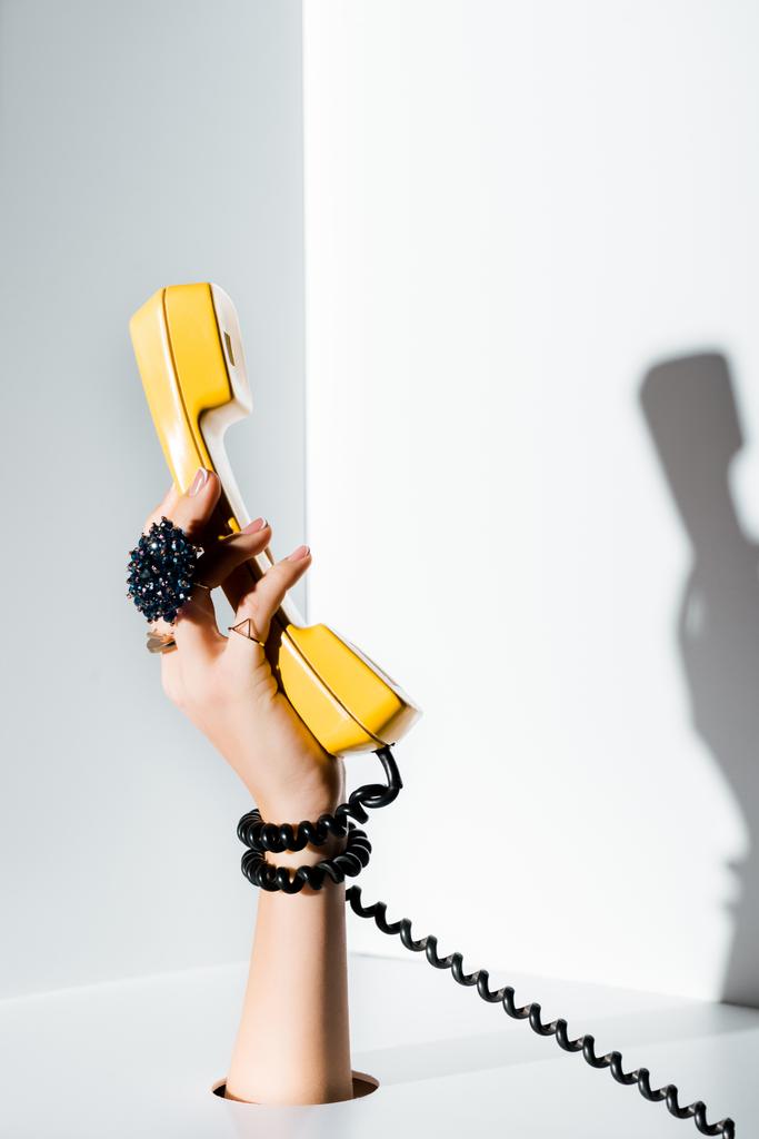 cropped image of girl holding yellow handset of retro telephone in hand through hole on white - Photo, Image