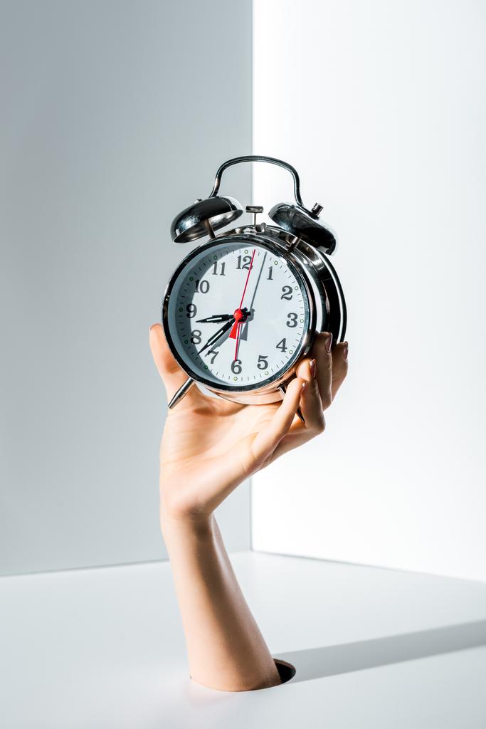 cropped image of woman holding retro styled alarm clock in hand through hole on white - Photo, Image