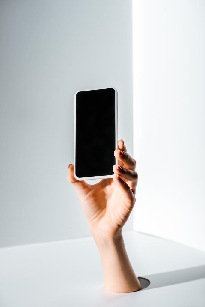 cropped image of woman holding smartphone with blank screen in hand through hole on white - Photo, Image
