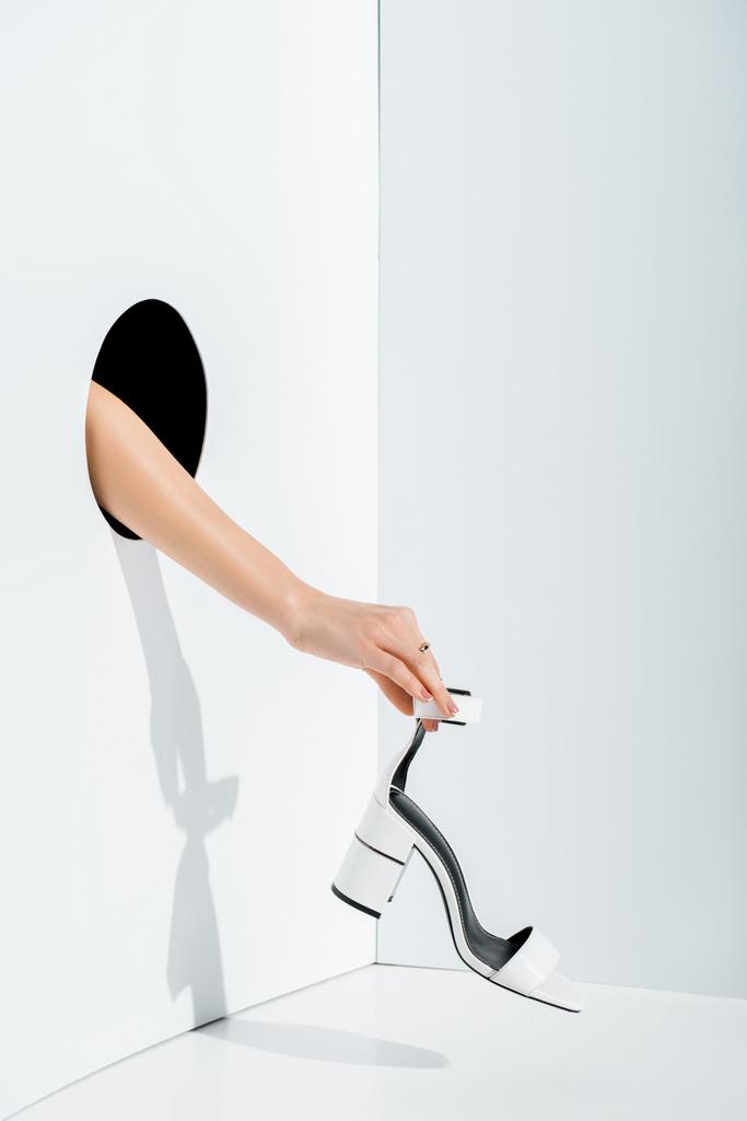обрізане зображення дівчини, що тримає білий високий каблук в руці через отвір на білому
 - Фото, зображення