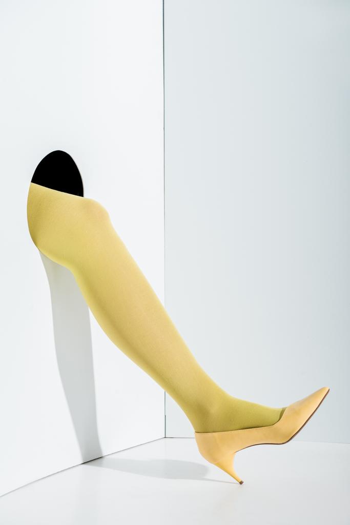 cropped image of woman showing leg in yellow tights and high heel in hole on white - Photo, Image