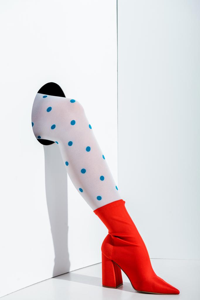 immagine ritagliata di ragazza mostrando gamba in calzamaglia bianca alla moda con puntini blu e scarpa rossa in foro sul bianco
 - Foto, immagini