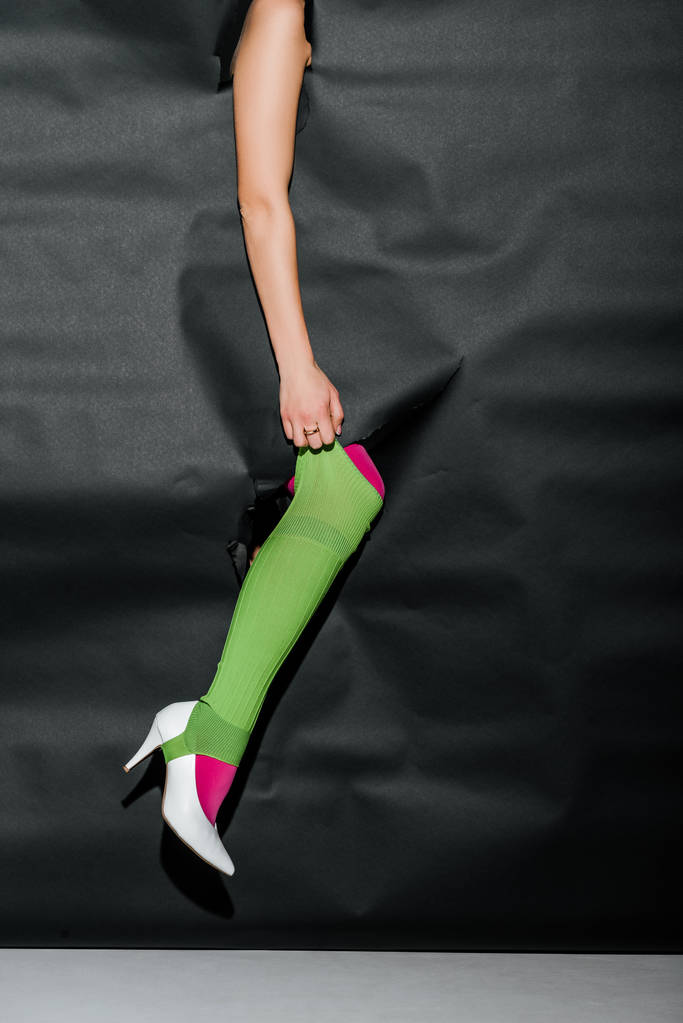 cropped image of girl showing leg in pink tights and white high heel through black paper, holding green gaiter - Photo, Image