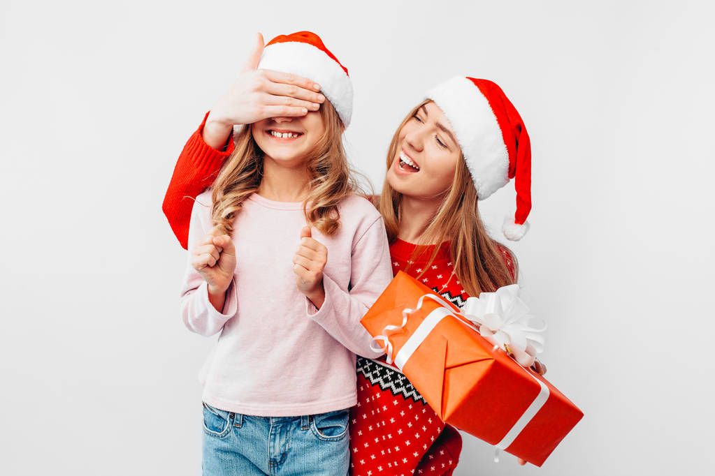 Córka z mamą w Santa Claus kapelusze i Christmas Swetry, Mama daje prezent na Boże Narodzenie do córki, na białym tle. Szczęśliwa rodzina koncepcja - Zdjęcie, obraz
