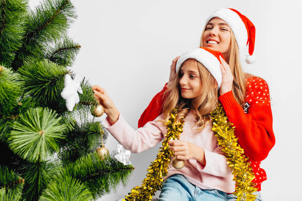 Mom and daughter, wearing Santa Claus hats, decorate the Christmas tree together, on a white background - Photo, Image