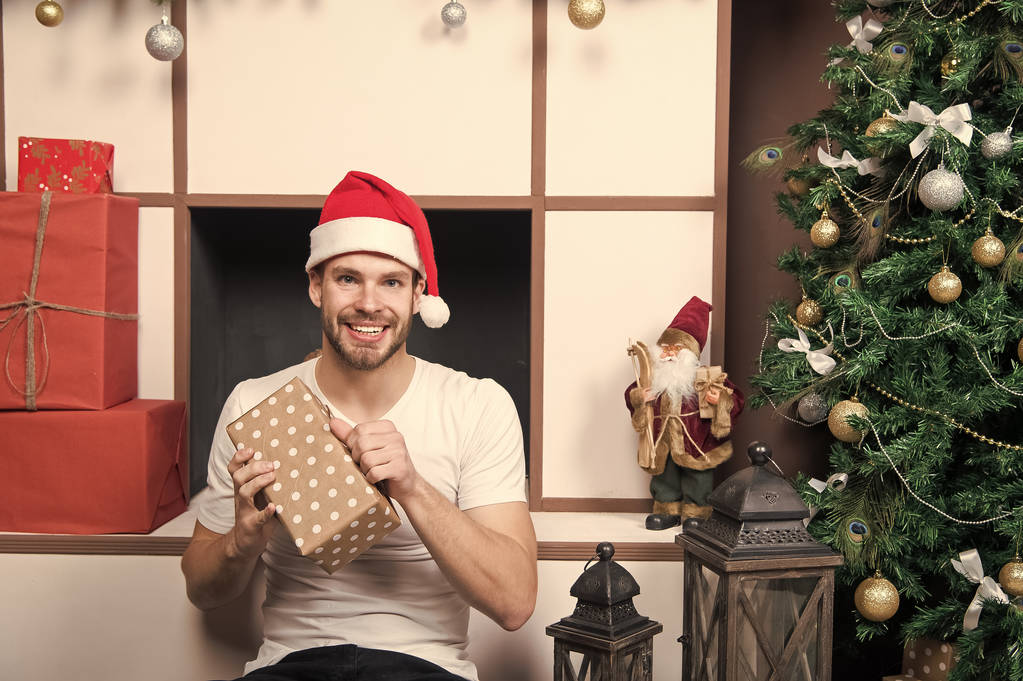 Санта-мужчина улыбается с подарочной коробкой на елке
 - Фото, изображение