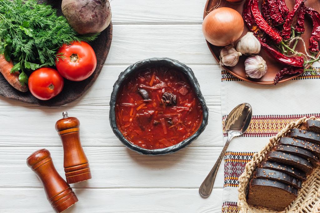 vista superior de deliciosa sopa tradicional de beterraba com talheres, ingredientes e pão de centeio no fundo de madeira branca
 - Foto, Imagem