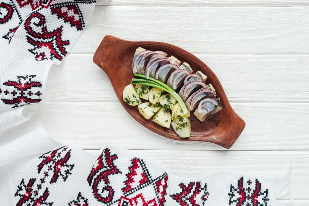 hareng mariné traditionnel avec pommes de terre et oignons dans une assiette en faïence avec serviette brodée sur fond blanc en bois
 - Photo, image