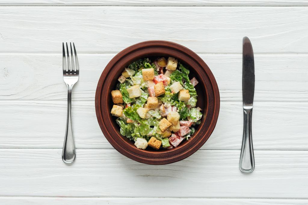 felülnézete a fehér fa háttér ízletes hagyományos Cézár saláta, burgonya, tálba és evőeszközök - Fotó, kép