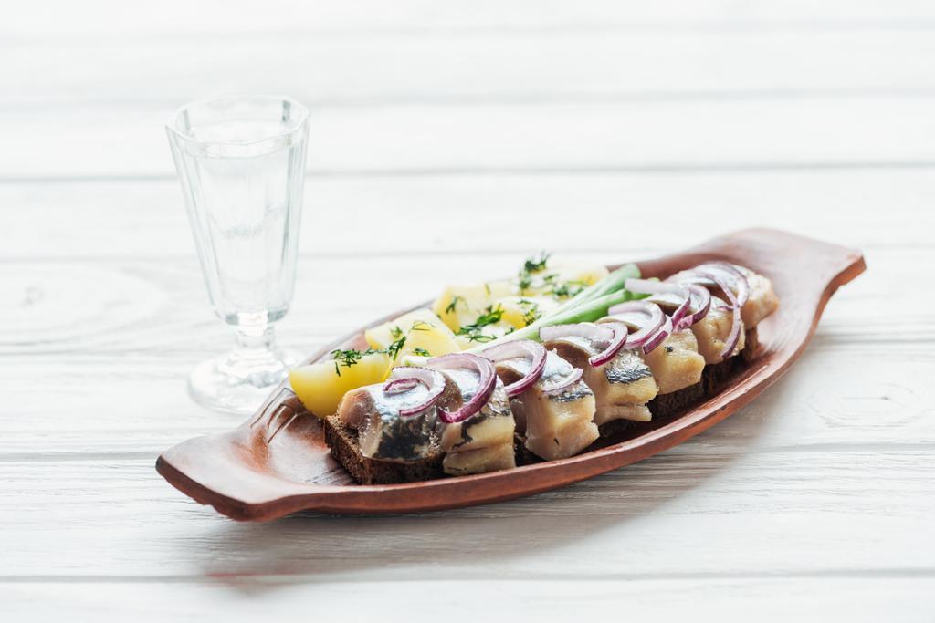 hareng mariné, pommes de terre et oignons dans une assiette en faïence avec verre de vodka sur fond de bois blanc
 - Photo, image