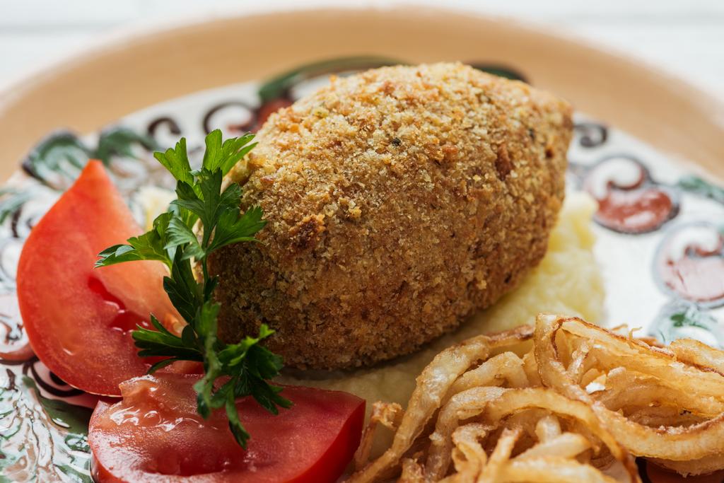 close up of chicken kiev with mashed potatoes, parsley, tomatoes and fried onions on plate with ornament - Photo, Image