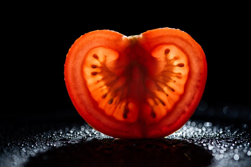 шматочок свіжого помідора з підсвічуванням на чорному фоні
 - Фото, зображення